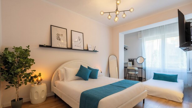 A modern bedroom with a bed, bedside tables, a potted plant, a desk, and a TV. - ReRent Rooms 169 Medaglie D'oro (Rome)