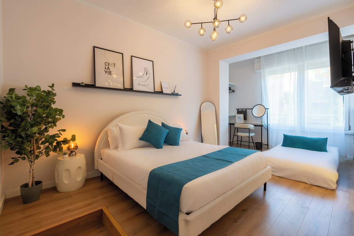 A modern bedroom with a bed, bedside tables, a potted plant, a desk, and a TV.