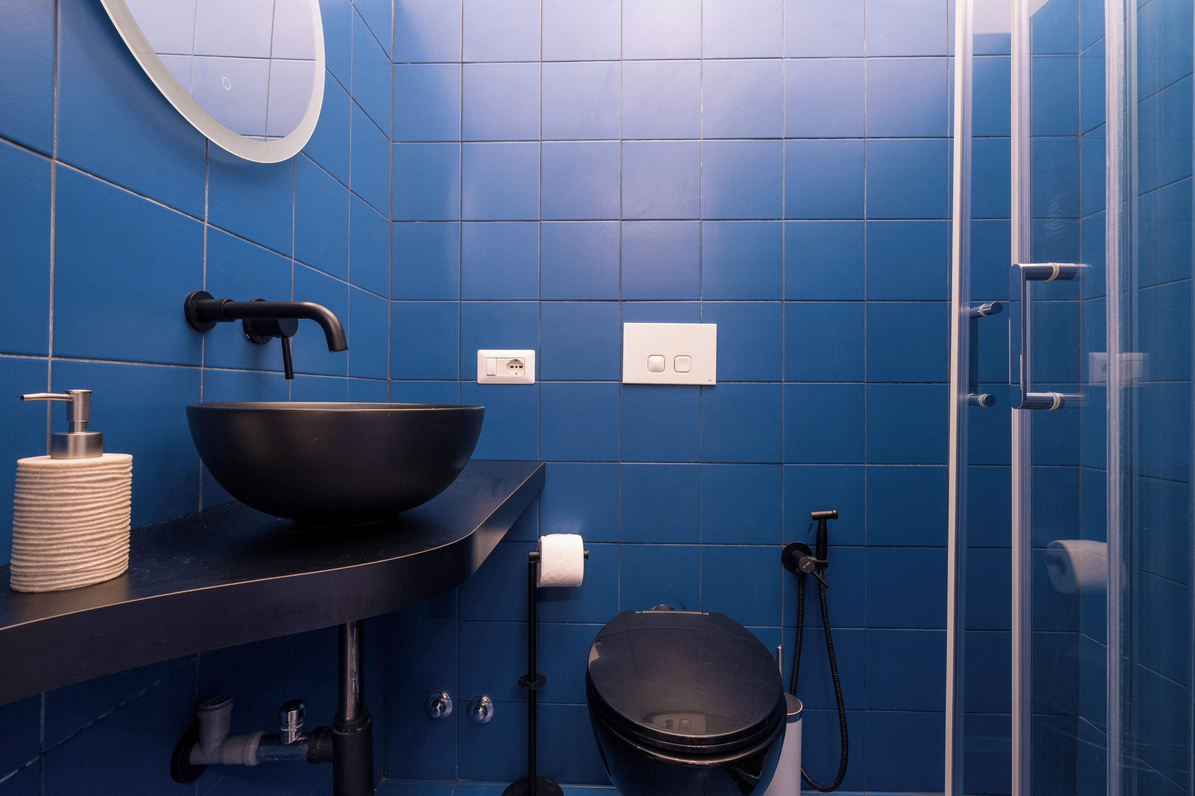 A bathroom with blue tiles, a black sink, a toilet, a shower, and a mirror.