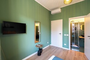 Quarto com televisão de tela plana, espelho, mesinha e porta para um banheiro com chuveiro.
