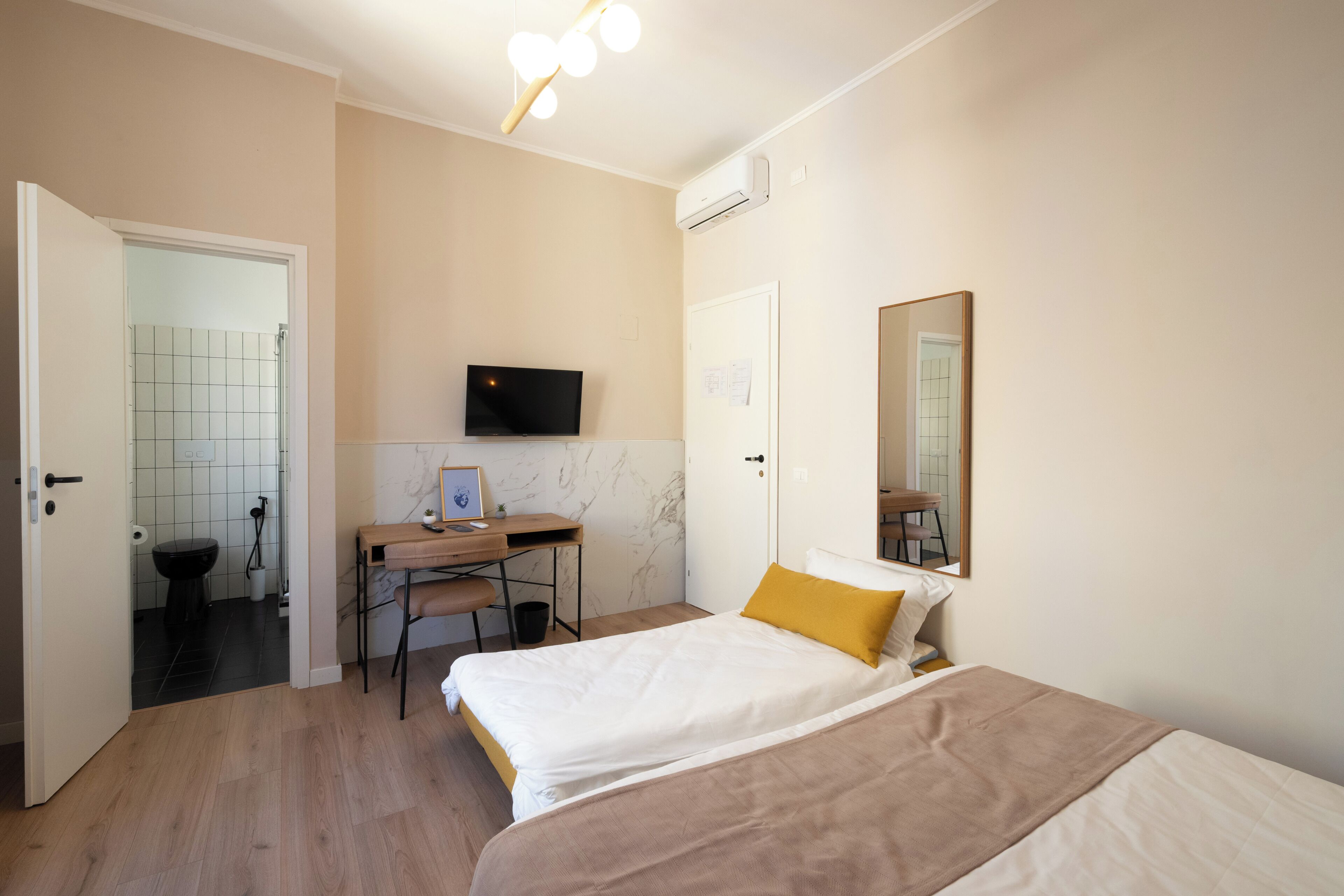 A bedroom with a bed, a desk, a chair, a television, and an air conditioning unit.