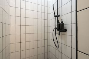 Zona de ducha con azulejos, cabezal de ducha manual y grifo empotrado.