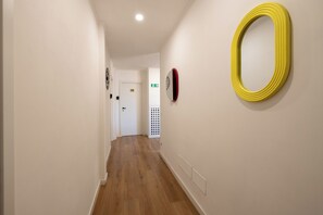 Um corredor com piso de madeira, paredes brancas e um espelho oval amarelo à direita.