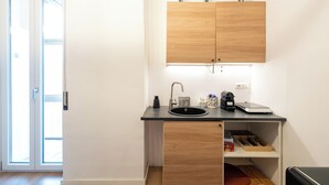 A compact kitchen with a wooden cabinet, a black countertop, a sink, and a small shelf with kitchen items. - ReRent Rooms 169 Medaglie D'oro (Rome)