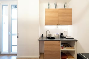 Una cocina compacta con un mueble de madera, una encimera negra, un lavabo y una pequeña estantería con utensilios de cocina.