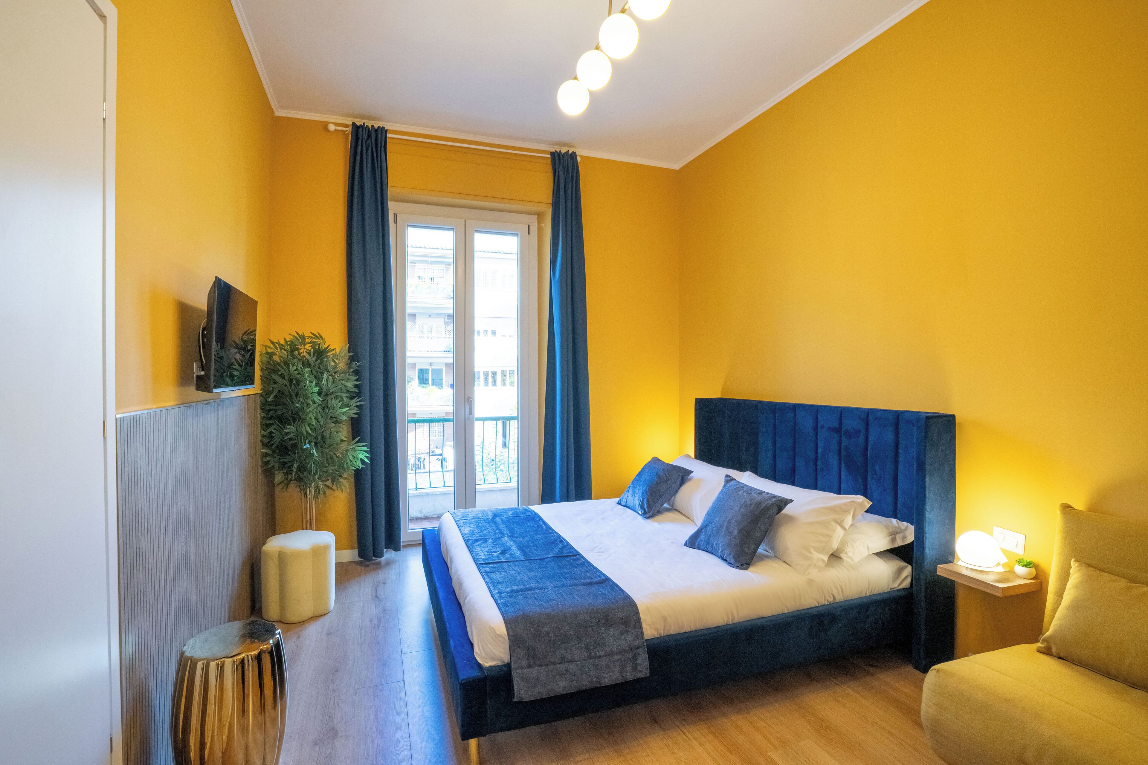 A bedroom with a bed, a TV, a plant, and a window with curtains.