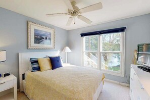 Un dormitorio con cama, ventilador de techo, ventana con vistas, mesita de noche y cómoda.