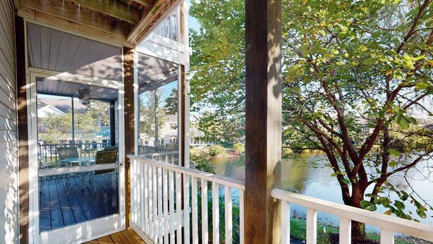 Un terrazzo in legno con ringhiera bianca, una porta in vetro e vista su un lago e alberi.