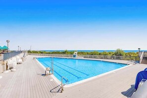 Una piscina con agua cristalina azul, rodeada por una cubierta de madera y una barandilla de metal.