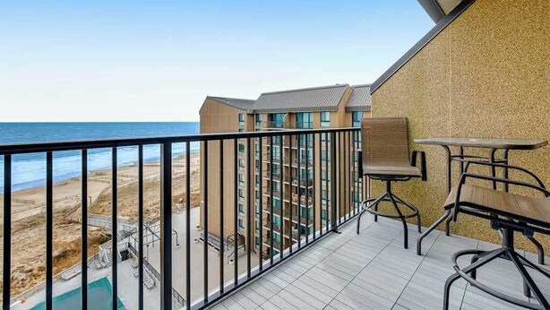 Ein Balkon mit Blick auf den Strand, ein Pool und ein mehrstöckiges Gebäude.