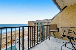 Ein Balkon mit Blick auf den Strand, ein Pool und ein mehrstöckiges Gebäude.