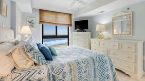 Ein Schlafzimmer mit Bett, Deckenventilator, Fernseher, Kommode, Spiegel und Meerblick.