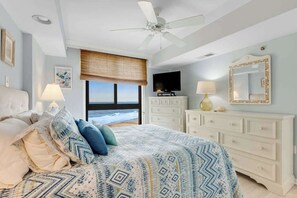 A bedroom with a bed, a ceiling fan, a television, a dresser, a mirror, and a view of the ocean. - Sea Colony Ocean 9th floor condo w/ gym, elevator, and shared sauna (Bethany Beach)