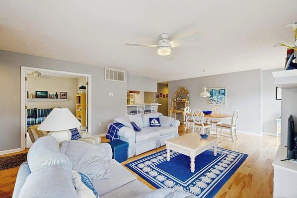 A living room with a sofa, coffee table, and a dining area with chairs and a table. - Sea Colony Tennis 1st-floor condo sauna & pool (Bethany Beach)