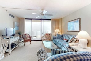 A hotel room with a television, a ceiling fan, a sofa, a coffee table, and a balcony with curtains. - Sea Colony Ocean 8th floor condo w/ free WiFi, shared sauna, and tennis court (Bethany Beach)