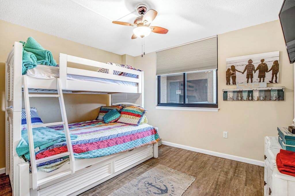 Ein Schlafzimmer mit Etagenbetten, einem Deckenventilator, einem Fenster mit Jalousien und einem Familienbild an der Wand.