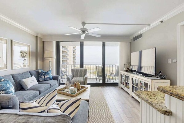 A living room with a sofa, a coffee table, a TV, and a balcony with a view. - Sea Colony Ocean 4th floor condo w/ free WiFi, balcony, and basketball court (Bethany Beach)