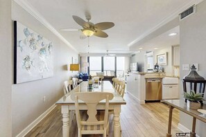 A dining area with a long table, chairs, a ceiling fan, and a kitchen area with appliances. - Sea Colony Ocean 4th floor condo w/ free WiFi, balcony, and basketball court (Bethany Beach)