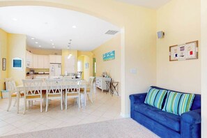 A living room with a blue sofa and a dining area with a white table and chairs. - Bayside Resort house w/ basketball court, fireplace, gym, and golf on-site (Selbyville)