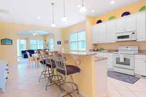A kitchen with white cabinets, a microwave, and a stove. There are bar stools and a dining table. - Bayside Resort house w/ basketball court, fireplace, gym, and golf on-site (Selbyville)