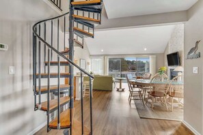 Ein modernes Interieur mit einer Wendeltreppe, einem Essbereich mit Holzsesseln und einem großen Fenster mit Blick.
