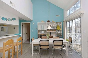 A modern kitchen with a white countertop, wooden chairs, and a blue accent wall. - Sea Colony Tennis 2nd floor condo w/ shared sauna, pool, and basketball court (Bethany Beach)