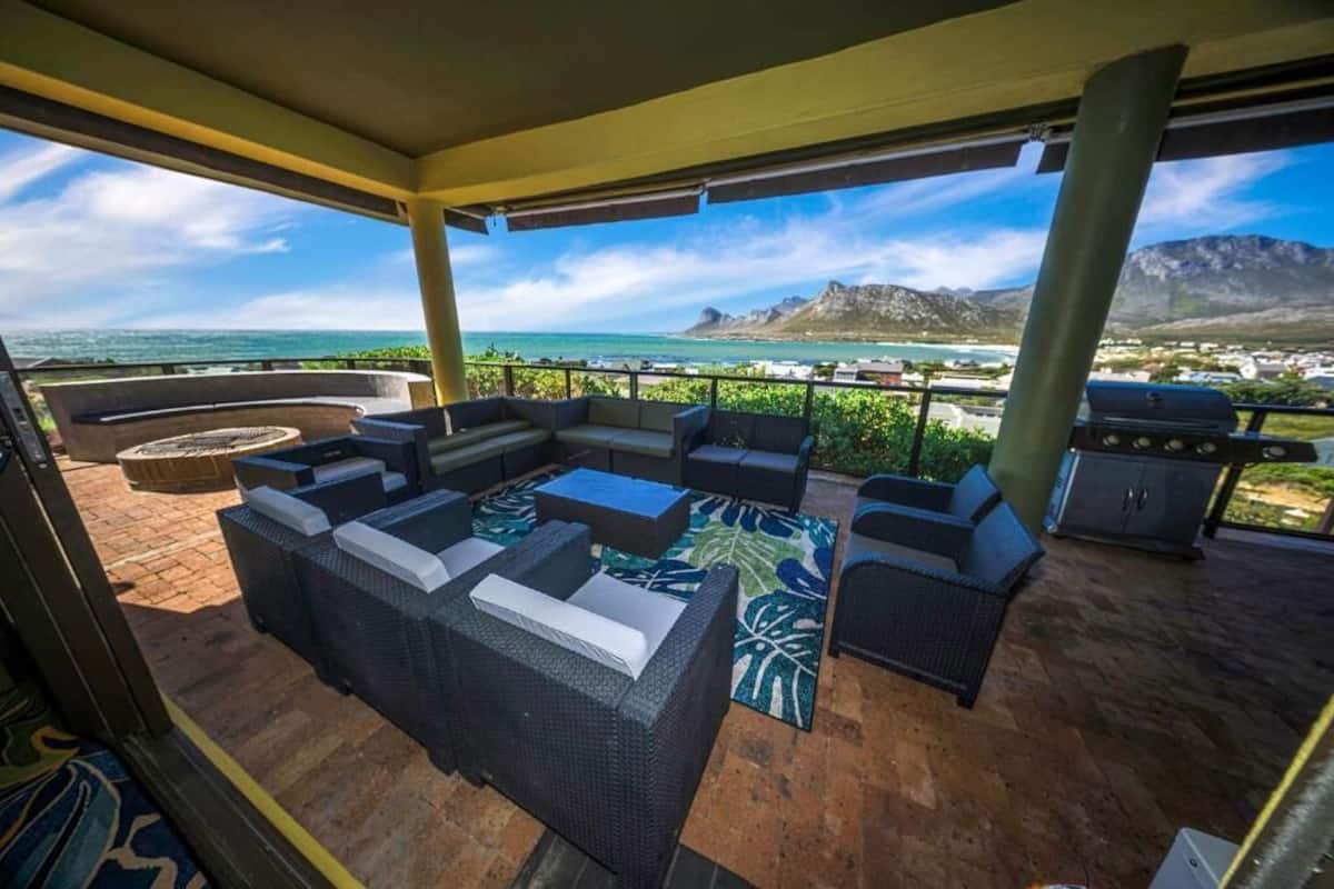 An outdoor patio with wicker furniture, a grill, and a view of the ocean and mountains.