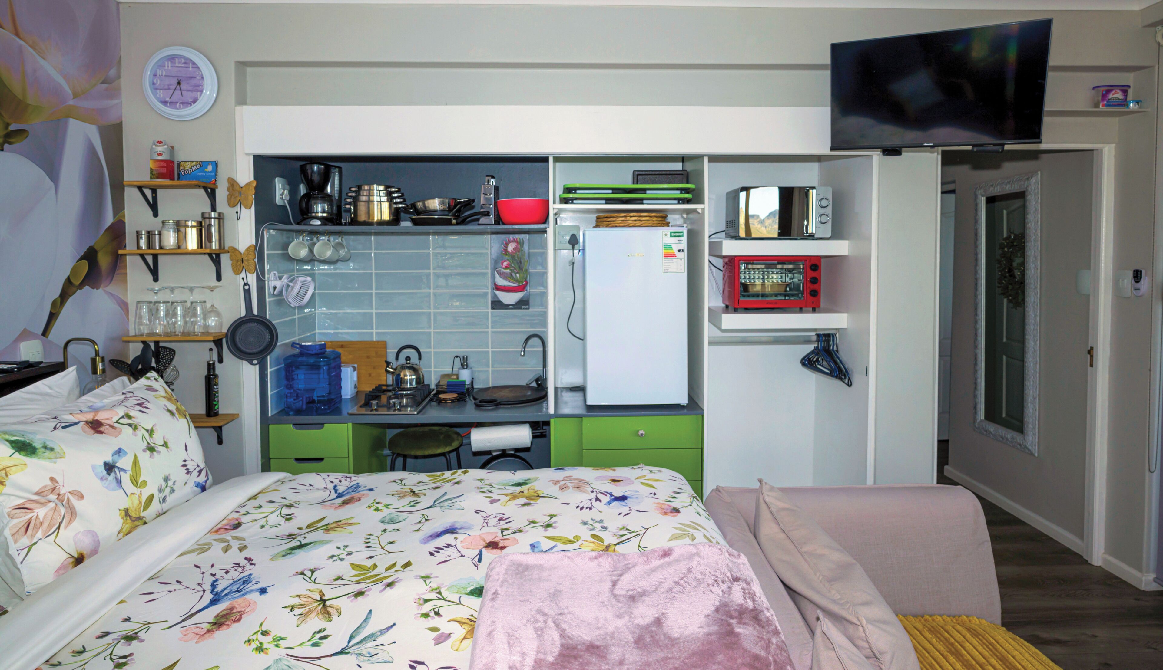 A compact room with a bed, kitchenette, and a TV.