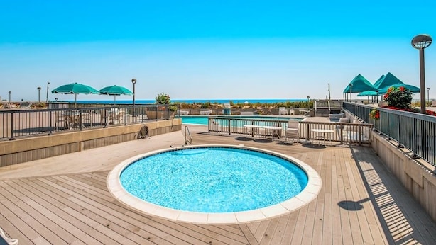 A pool area with a wooden deck, lounge chairs, and umbrellas. - Sea Colony Tennis 2nd floor condo w/ gym, shared sauna, and balcony (Bethany Beach)