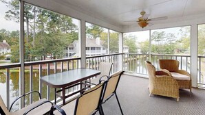 A covered outdoor area with a table and chairs, large windows, and a view of a water body and houses. - Sea Colony Tennis 2nd floor condo w/ gym, shared sauna, and balcony (Bethany Beach)