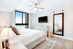 A bedroom with a bed, a ceiling fan, a TV, a large mirror, and a view of the beach. - Sea Colony Ocean 5th floor condo w/ balcony, shared sauna, and tennis court (Bethany Beach)