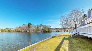 Une propriété située au bord de l’eau, avec une pelouse, une clôture blanche et des arbres en arrière-plan.