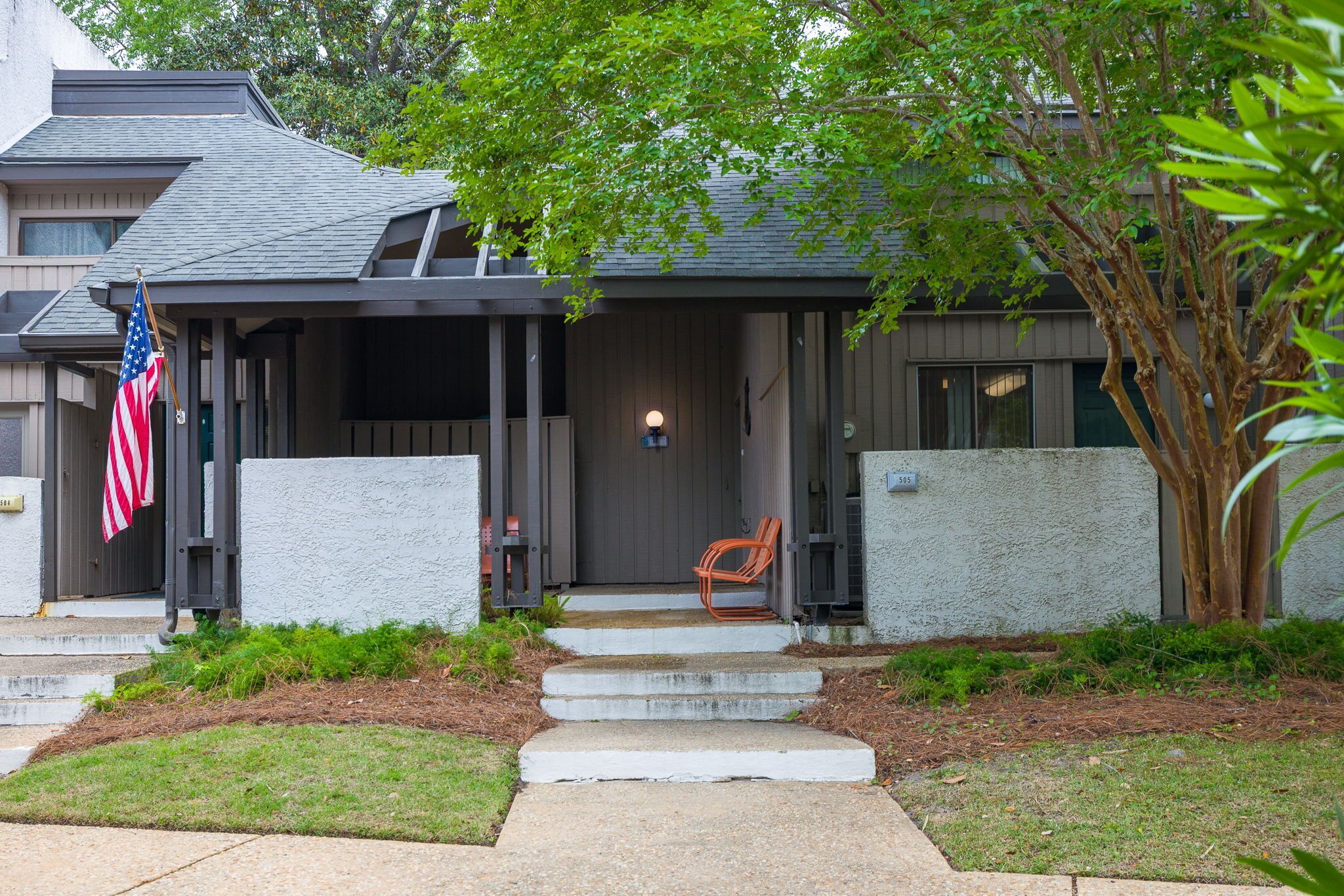 A residential house with a porch, steps leading to the entrance, and an American flag.