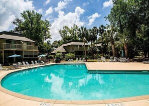 A swimming pool with lounge chairs and umbrellas, surrounded by buildings and trees. - 505 Tennismaster | 3 Bedrooms | Dog Friendly | Walk to Beach | STR #075784 (Hilton Head Island)