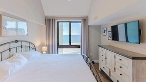 Una camera da letto con un letto, una ventola a soffitto, una finestra con tende, un comò e una TV appesa al muro.