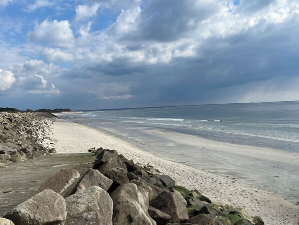 Ein Strand mit großen Felsen im Vordergrund und einem weiten Sandstrand.