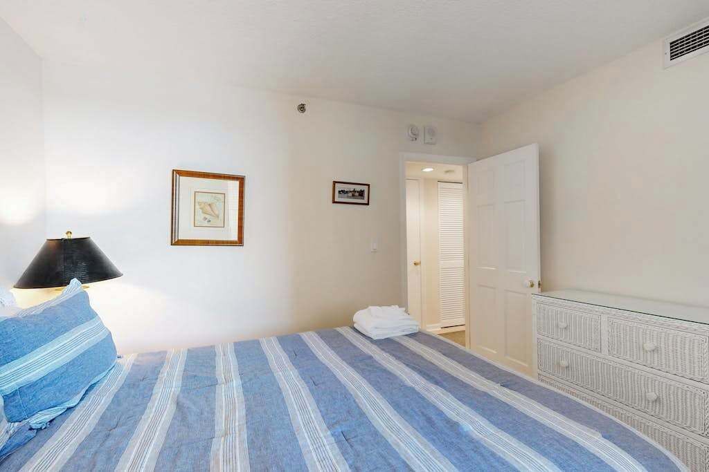 A bedroom with a bed, a nightstand, a dresser, a framed picture, and a door leading to another room.