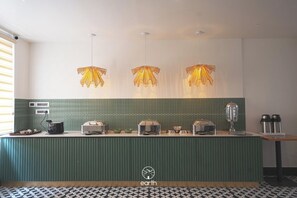 Cozinha de hotel com bancada verde, três luminárias pendentes e diversos eletrodomésticos.