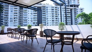 An outdoor seating area with tables and chairs, potted plants, and a view of high-rise buildings. - Earth Hotels Hebbal (Bengaluru)