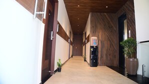 A hallway with wooden walls, a tiled floor, and a refrigerator with a water dispenser. - Earth Hotels Hebbal (Bengaluru)