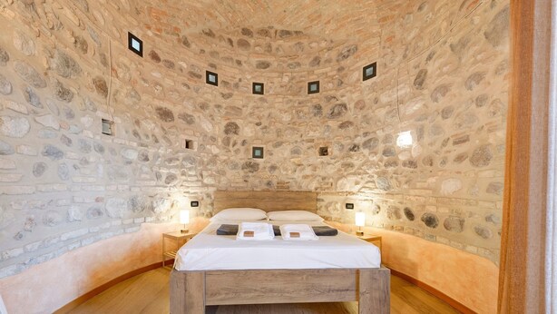 A stone-walled bedroom with a wooden bed, two bedside tables, and a nightstand.