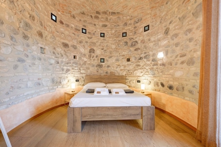 A stone-walled room with a wooden bed, two bedside tables, and a small window.. Apartment 'Casa Dolce Casa Al Castello' with Lake View, Wi-Fi and Air Conditioning