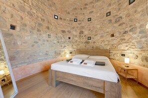 Una stanza con pareti in pietra, un letto, un comodino e una piccola finestra.