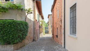 A narrow alleyway with cobblestone pavement, flanked by buildings with brick walls and windows with metal grilles.