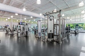 Ein großzügiger Fitnessraum mit verschiedenen Trainingsgeräten, einer hohen Decke mit Industrielaustrahlung und großen Fenstern.