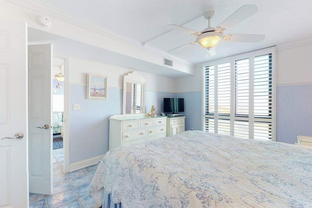 A bedroom with a bed, dresser, television, and a ceiling fan.