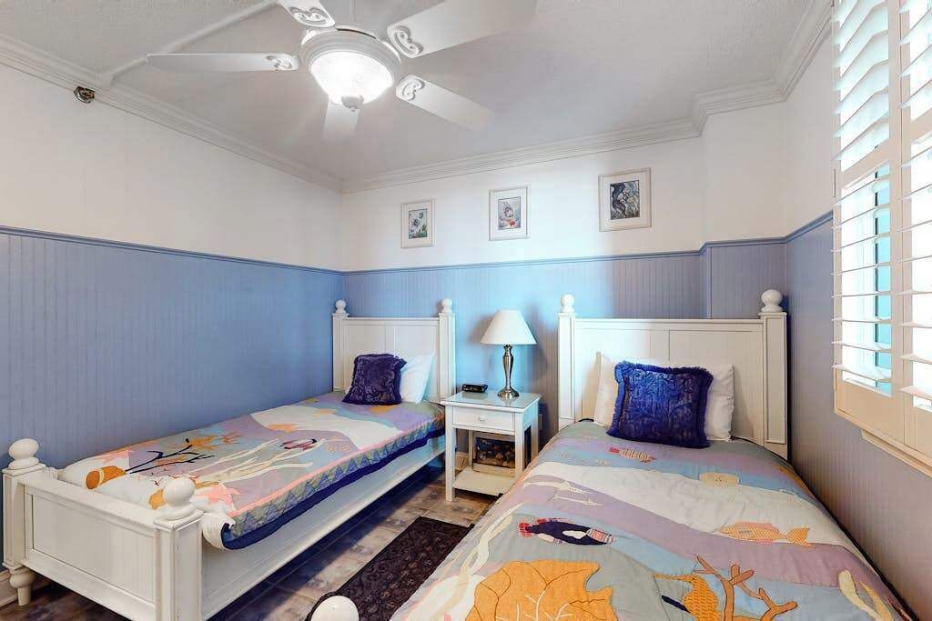 A bedroom with two beds, a ceiling fan, a nightstand, and a window with blinds.
