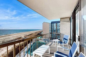 Un balcón con vista a la playa y al océano, sillas reclinables blancas y una piscina.