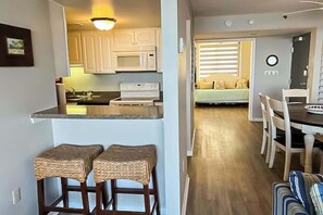 A kitchen with white cabinets, a microwave, and a stove. There are two bar stools and a dining table with chairs. - Sea Colony Ocean 8th floor condo w/ pool, balcony, and tennis court (Bethany Beach)