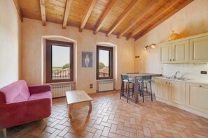 Ein gemütliches Interieur mit Holzboden, einem rosa Sofa, einem kleinen Tisch, einer Küchenzeile mit Barhocker und Blick durch ein Fenster.
